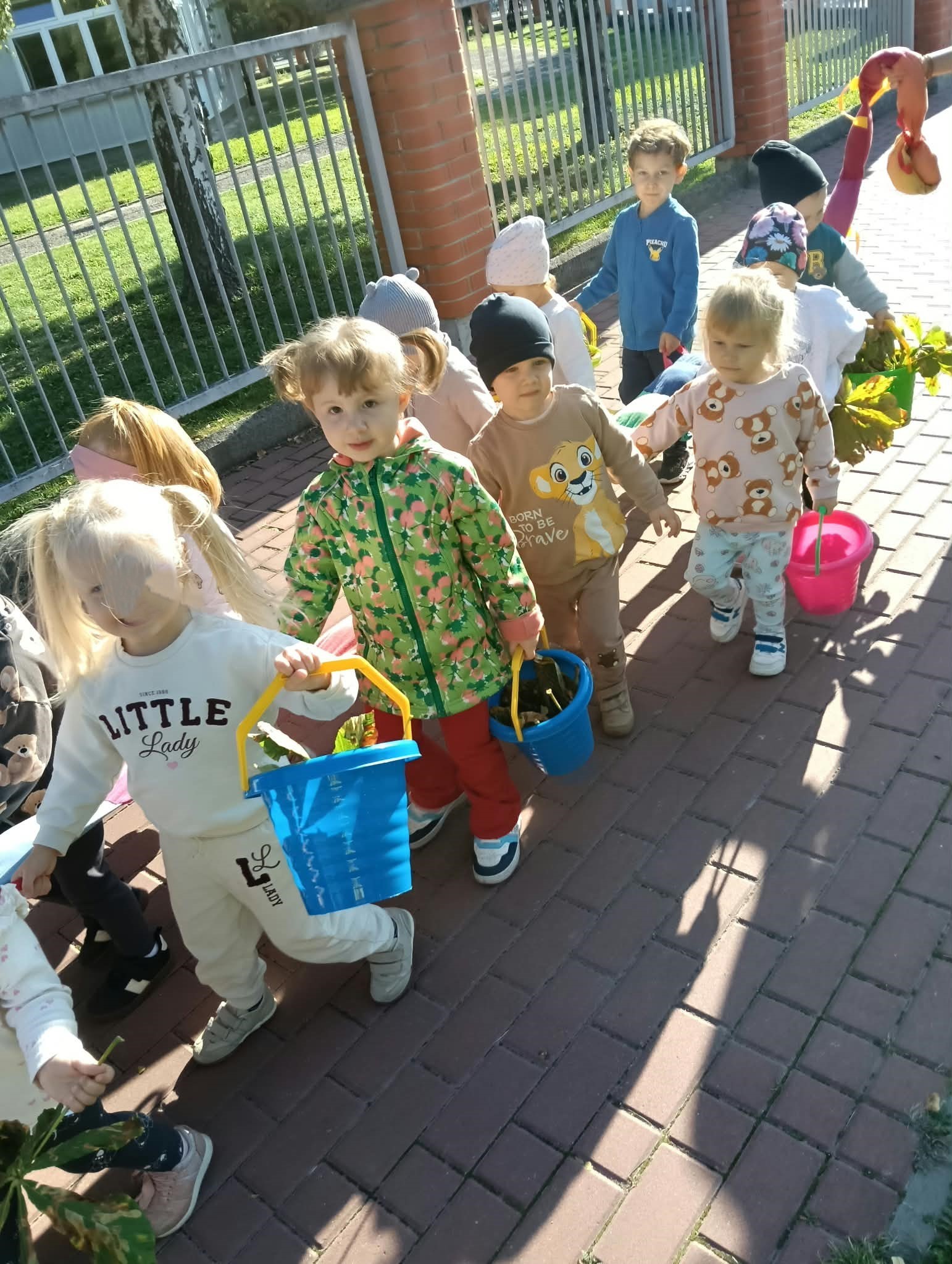 Zdjęcie przedstawia dzieci podczas spaceru i szukania darów jesieni